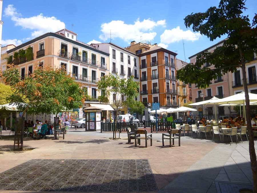 Terrazas y edificios con balcones alrededor de una plaza arbolada del barrio de Malasaña