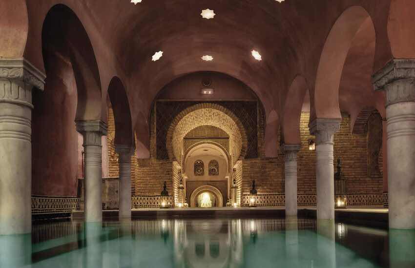 Sala abovedada de un baño árabe con arcos de herradura y una piscina de agua turquesa