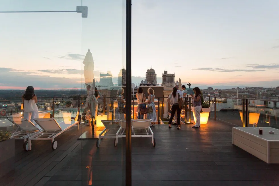 Terraza de azotea con tumbonas y gente al atardecer sobre los tejados del centro de Madrid