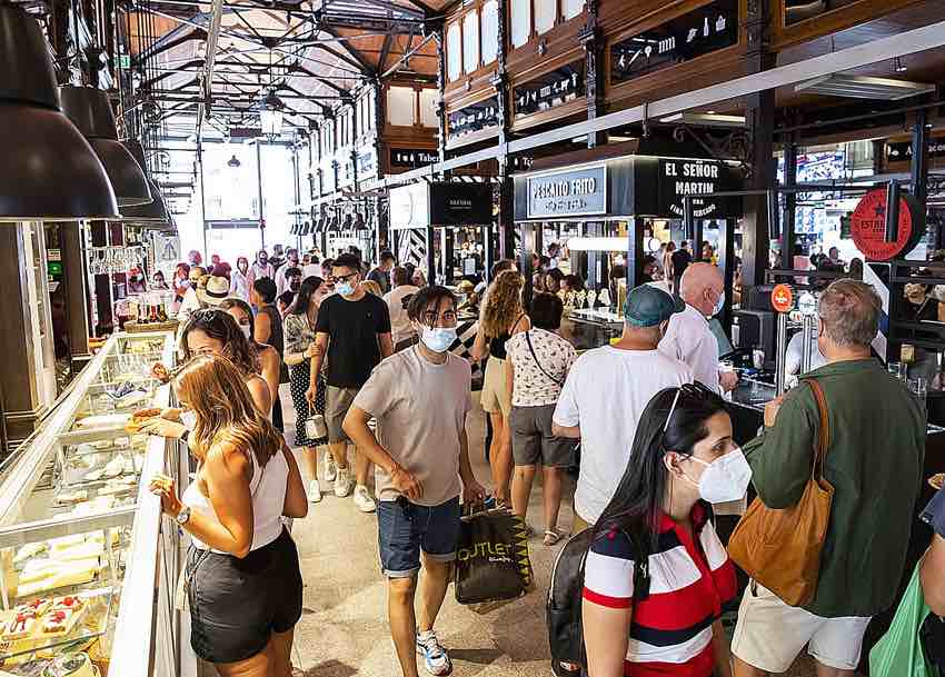 Pasillo del Mercado de San Miguel lleno de gente entre los puestos, bajo su estructura de hierro