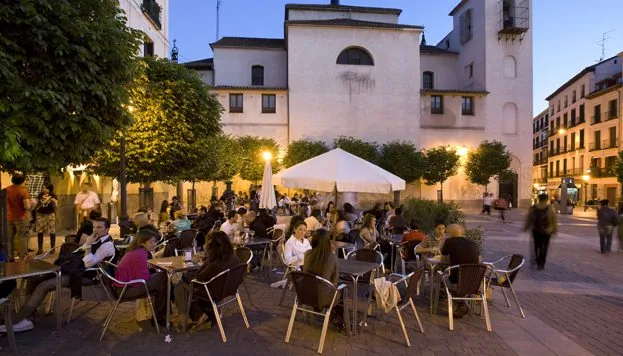 Terrazas llenas al anochecer en la Plaza de San Ildefonso, frente a la fachada blanca de la iglesia