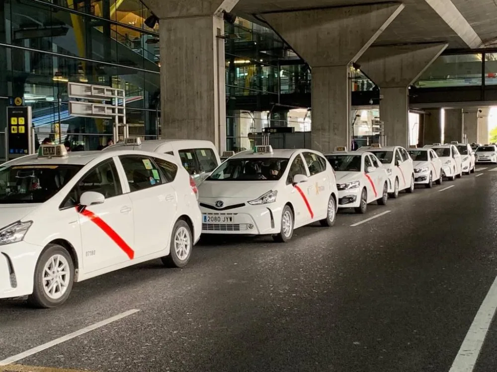 Fila de taxis blancos con la franja roja de Madrid esperando bajo la marquesina del aeropuerto