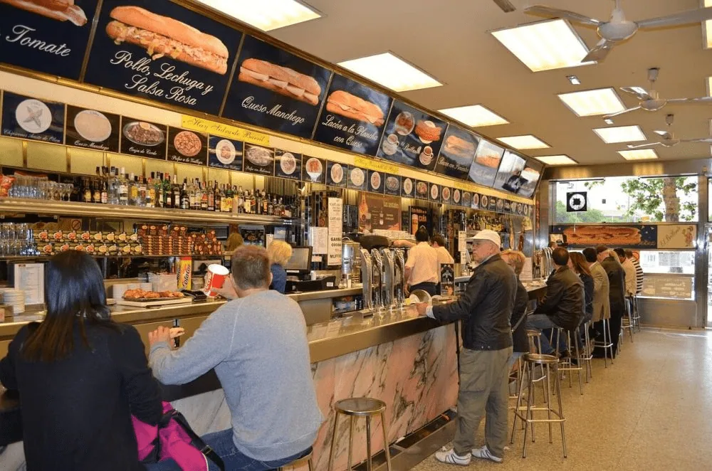Clientes en la barra de un bar de bocadillos, con las fotos de los bocadillos sobre la pared