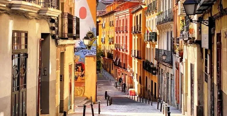 Calle empinada con fachadas de colores, balcones y grafitis en un barrio del centro de Madrid
