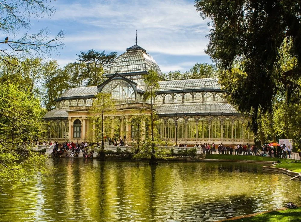 El Palacio de Cristal del Retiro reflejado en su estanque, con visitantes en la escalinata