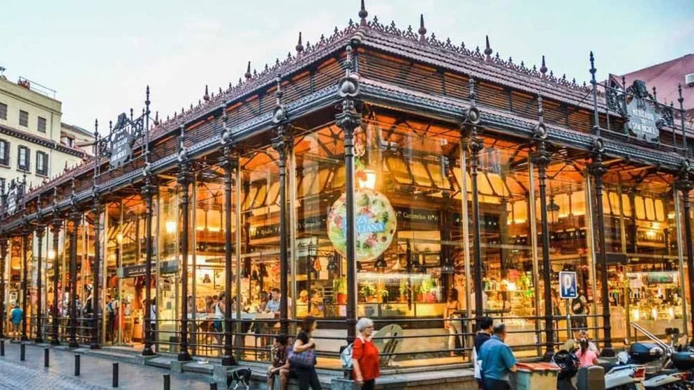 Fachada acristalada del Mercado de San Miguel iluminada al anochecer