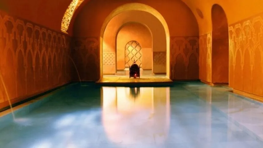 Sala de un baño árabe con paredes anaranjadas, un gran arco de herradura y la piscina en calma